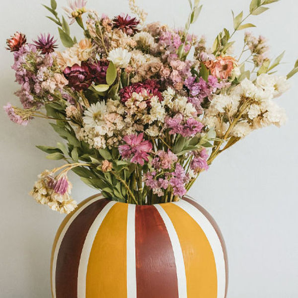 Bunter Blumenstrauß aus getrockneten Blüten in einer gestreiften Vase in warmen Gelb- und Brauntönen