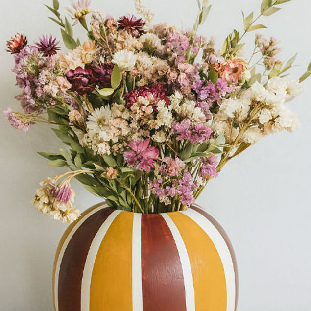 Bunter Blumenstrauß aus getrockneten Blüten in einer gestreiften Vase in warmen Gelb- und Brauntönen