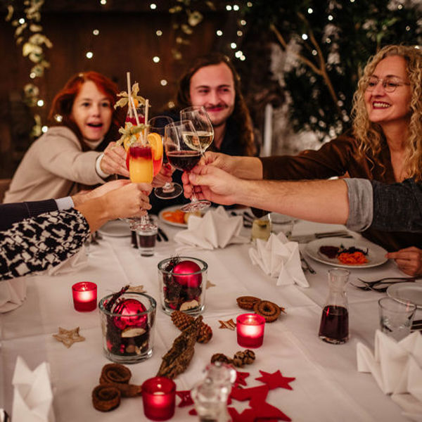 Drei Personen stoßen an einem festlich gedeckten Tisch mit Glühwein an. Kerzen, Weihnachtsdekoration und warme Lichter sorgen für eine stimmungsvolle Atmosphäre