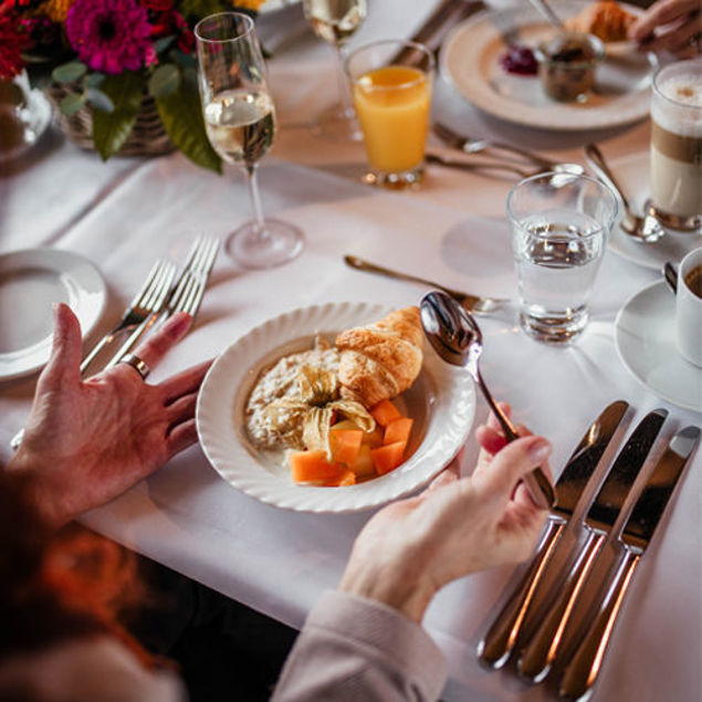 Teller mit Croissant, Bircher Müsli, Melonenstücken und Aufstrich auf gedecktem Tisch mit Orangensaft, Wasser und Kaffee beim Erntedankbrunch